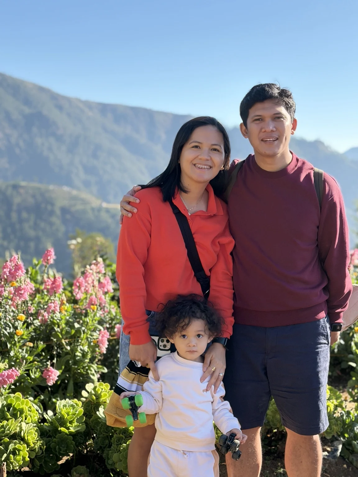Justin, Charlene and Simon together in a flower garden with mountains behind them