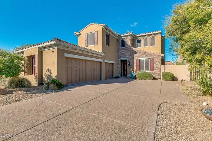 Two-story desert home with stone accents and a landscaped driveway